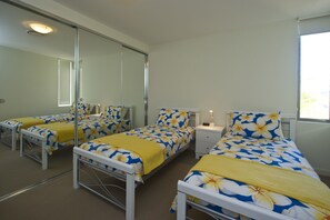 Una habitación de hotel con dos camas, cada una con una colcha de flores amarillas y azules, una mesita de noche con lámpara, y un espejo grande en una pared.