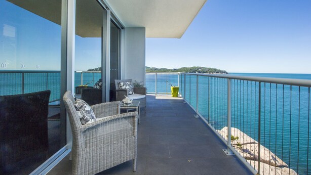 A balcony with wicker furniture, a glass railing, and a view of the sea. - 1 Bright Point Apartment 5404 (Nelly Bay)