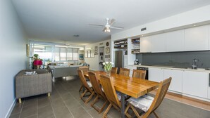A modern kitchen with white cabinets, a stainless steel refrigerator, and a dining area with a wooden table and chairs. - 1 Bright Point Apartment 5404 (Nelly Bay)