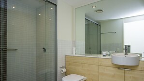 Un bany modern amb dutxa de vidre, un vàter blanc i un lavabo amb mirall a la part superior.