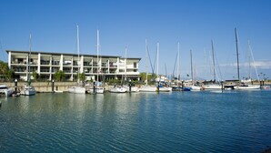 Un port esportiu amb diversos velers amarrats davant d'un edifici modern de múltiples pisos i balcons.