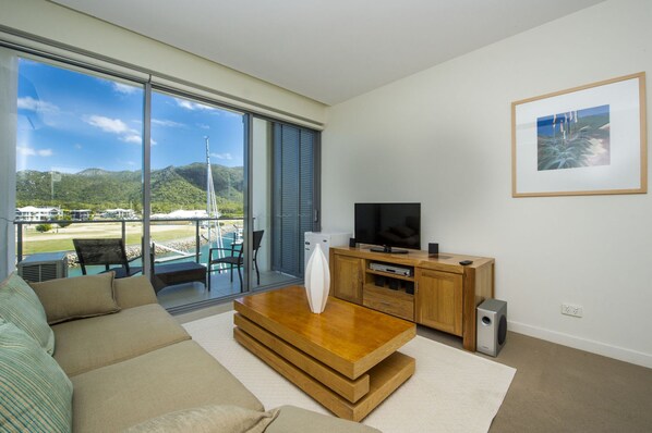 A modern living room with a large sliding glass door leading to a balcony with a view of a marina and mountains.