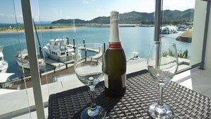 Een fles wijn en twee glaasjes op een tafel met uitzicht op een jachthaven en water.