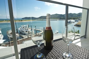 Une bouteille de vin et deux verres sur une table, avec vue sur une marina et sur l’eau.