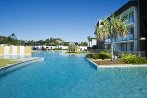 Une piscine bordée d’un bâtiment moderne d’un côté et d’un espace paysager agrémenté de palmiers de l’autre.