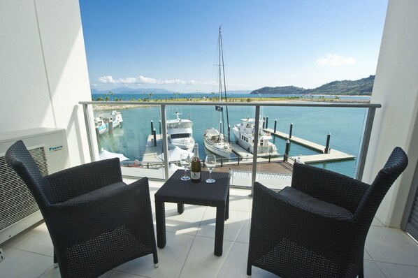 Un balcon avec deux fauteuils en osier et une petite table, donnant sur une marina où sont amarrés plusieurs bateaux.