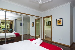 A hotel room with a bed, a red accent wall, a large mirror, and a bathroom visible through an open door. - Marramaninjie (Arcadia)