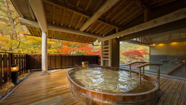 A wooden deck with a hot tub, wooden pillars, and a view of autumn foliage. - Hanamaki Onsen Kashoen (Hanamaki)