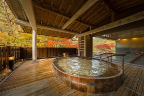Una terraza de madera con jacuzzi, pilares de madera y vistas a follaje otoñal.