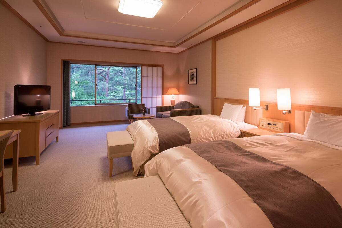 Ett hotellrum med två sängar, ett skrivbord, en tv och ett fönster med utsikt över tr äd.