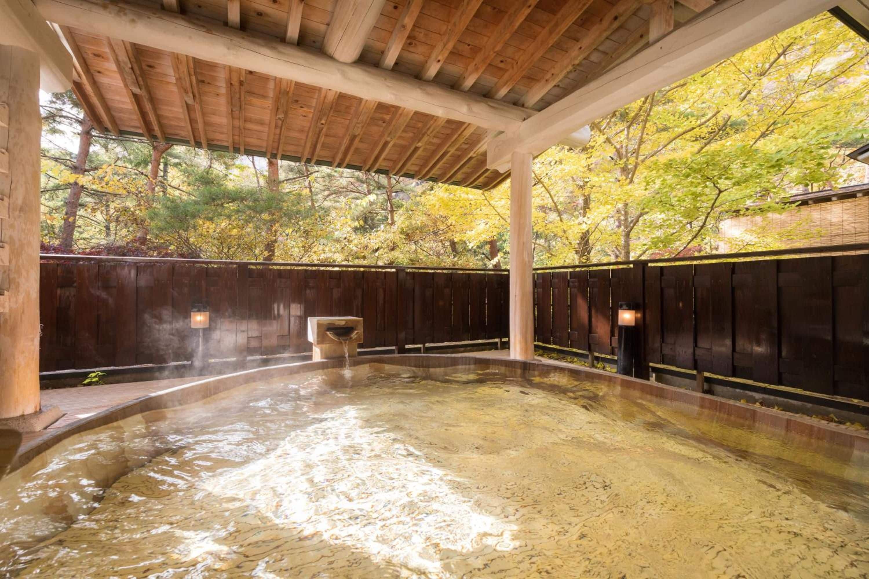Zona de baños termales con vigas de madera, suelo de piedra y vistas a árboles otoñales.
