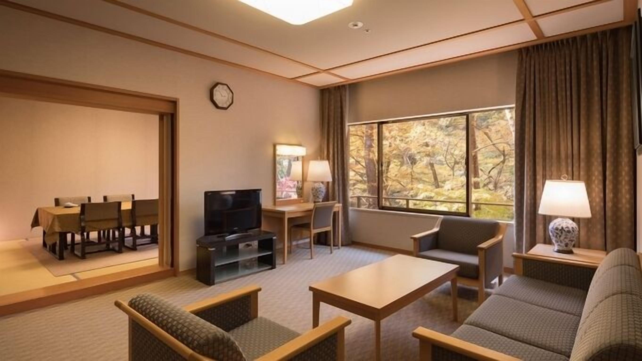 A hotel room with a sofa, a table, a TV, a desk, and a window with a view of trees.