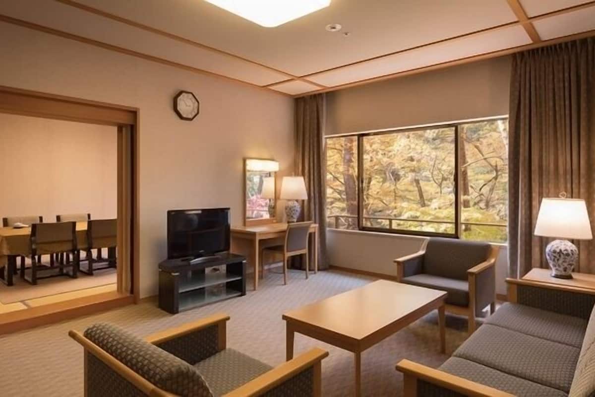 A hotel room with a sofa, a table, a TV, a desk, and a window with a view of trees.