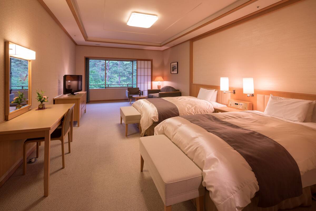 Ett hotellrum med två sängar, ett skrivbord, en TV och ett fönster med utsikt över träd.