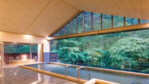 An indoor swimming pool with clear glass walls, a tiled floor, and a view of a forested area outside. - Hanamaki Onsen Kashoen (Hanamaki)