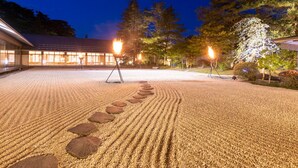 A serene garden with a gravel path leading to a building, surrounded by trees and illuminated by warm lights. - Hanamaki Onsen Kashoen (Hanamaki)