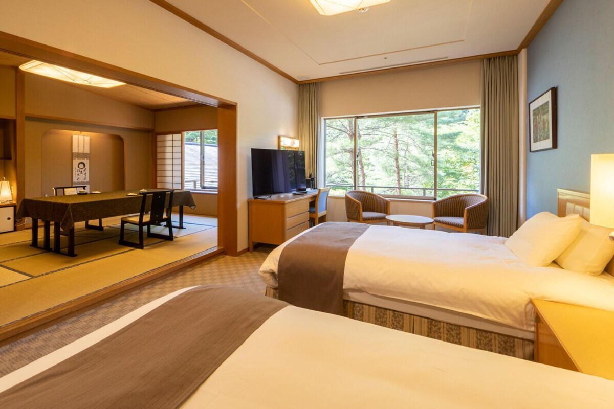 A hotel room with two beds, a desk with a TV, a dining table, and chairs.