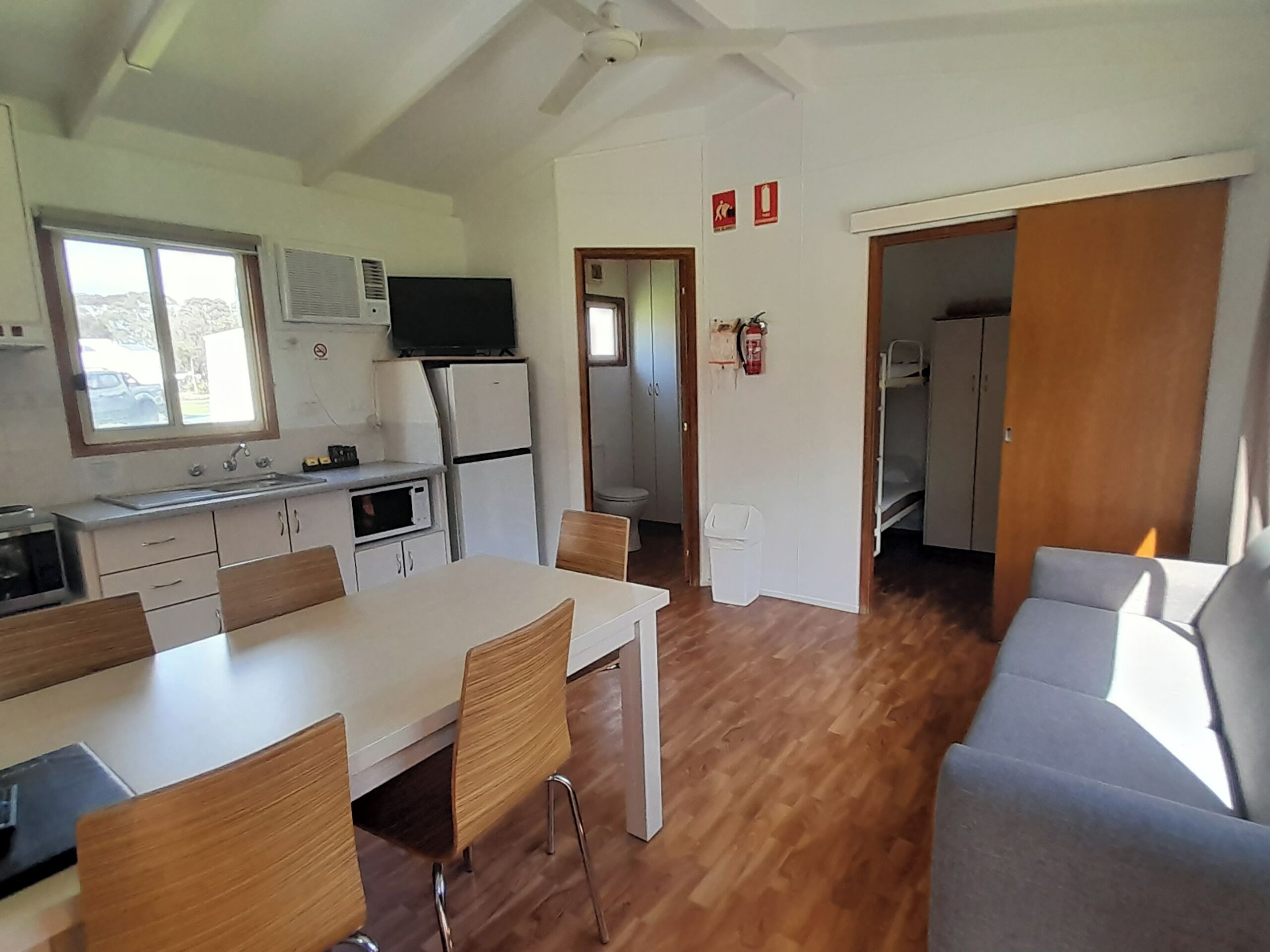 Cocina compacta con comedor, televisor y ventilador de techo.