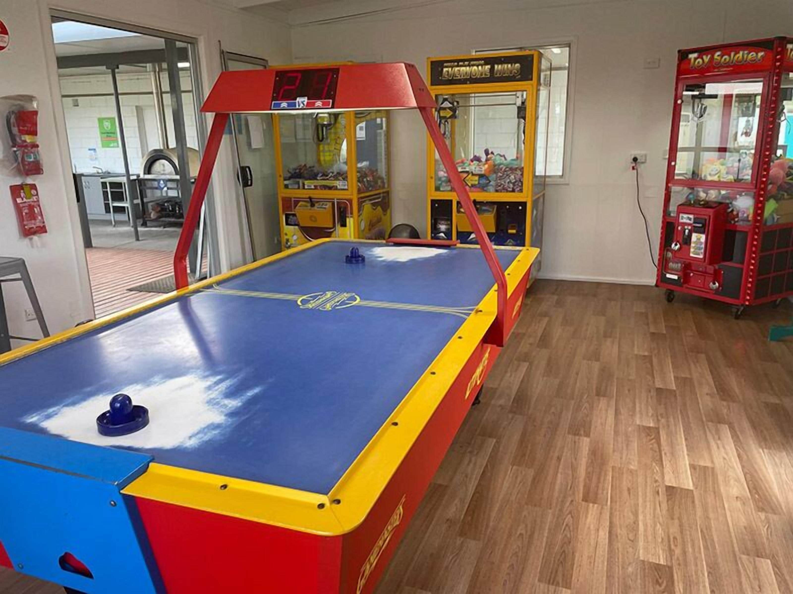 A pool table with a digital scoreboard, a claw machine, and a toy soldier vending machine in a room with wooden flooring.
