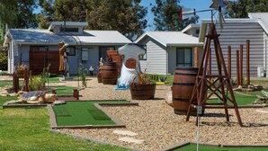 Il s’agit d’une propriété résidentielle dotée d’un jardin devant la maison, comprenant un mini-terrain de golf, un moulin à vent et un grand tonneau en bois.