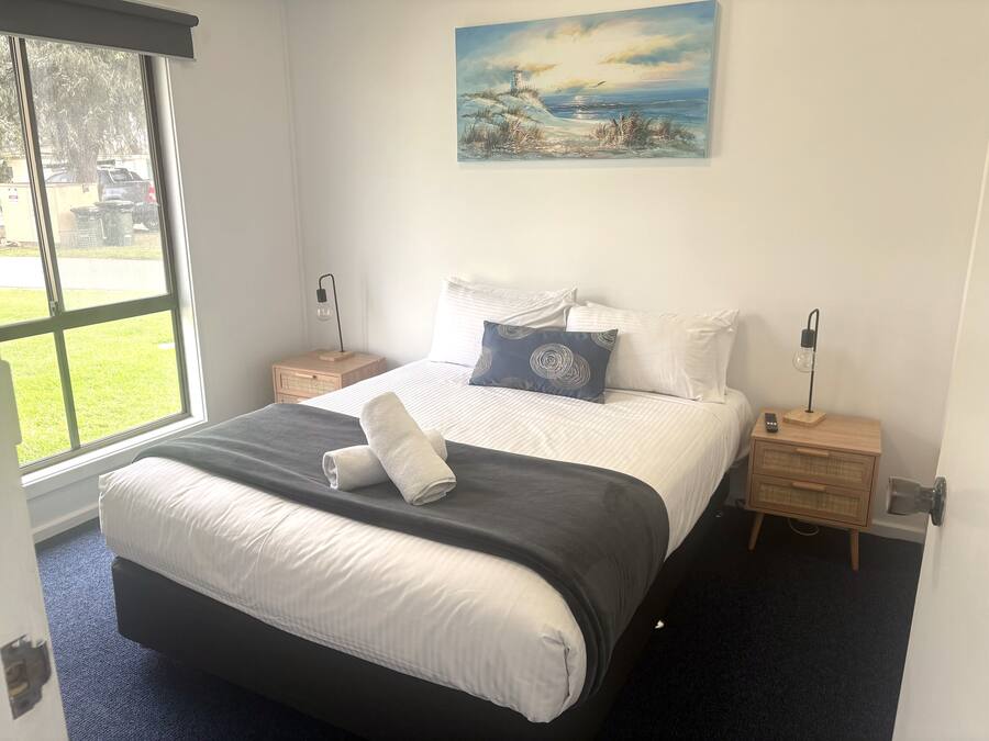 A bedroom with a large bed, a nightstand with a lamp, and a painting on the wall.