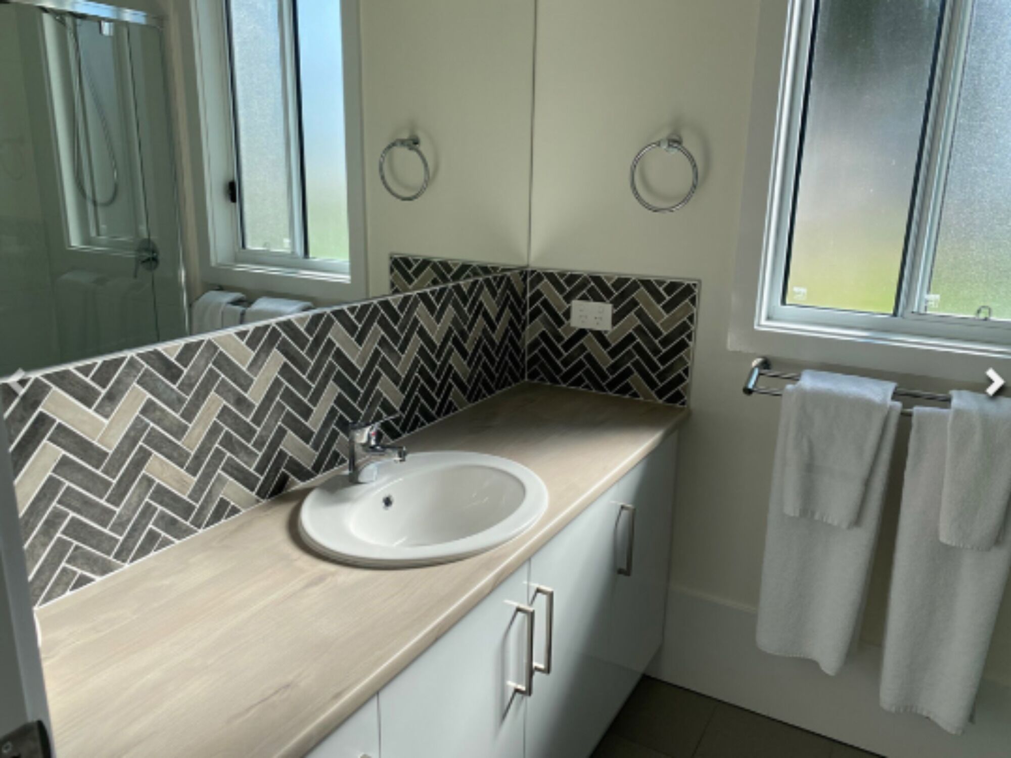 Un bagno con rivestimento a backsplash in mosaico a spina di pesce, un lavandino bianco e una finestra con porta asciugamani.
