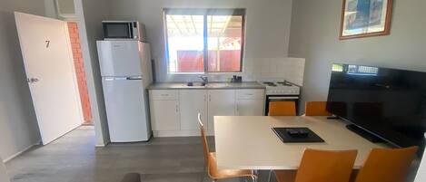 A compact kitchen with a refrigerator, microwave, stove, and sink. There is a dining area with a table and chairs, and a television on a stand.