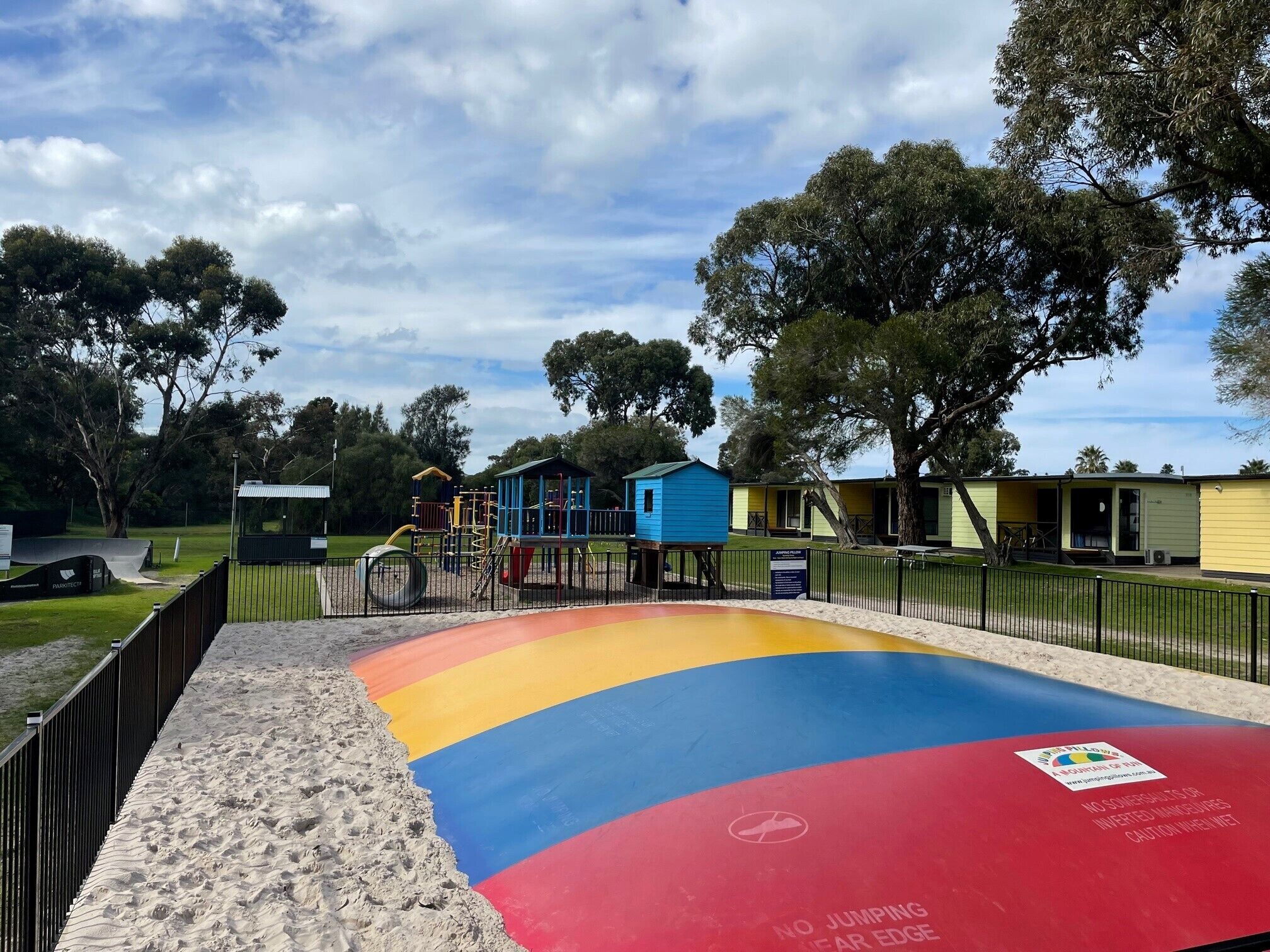 A playground with colorful play structures and a sandy area with a no-jumping warning sign.