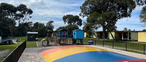 A playground with colorful play structures and a sandy area with a no-jumping warning sign.