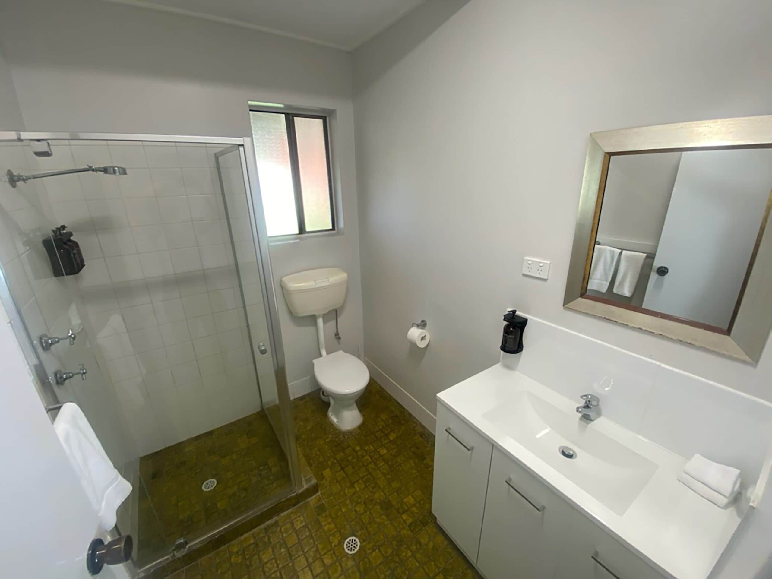 Un baño con ducha, inodoro, lavabo y espejo.