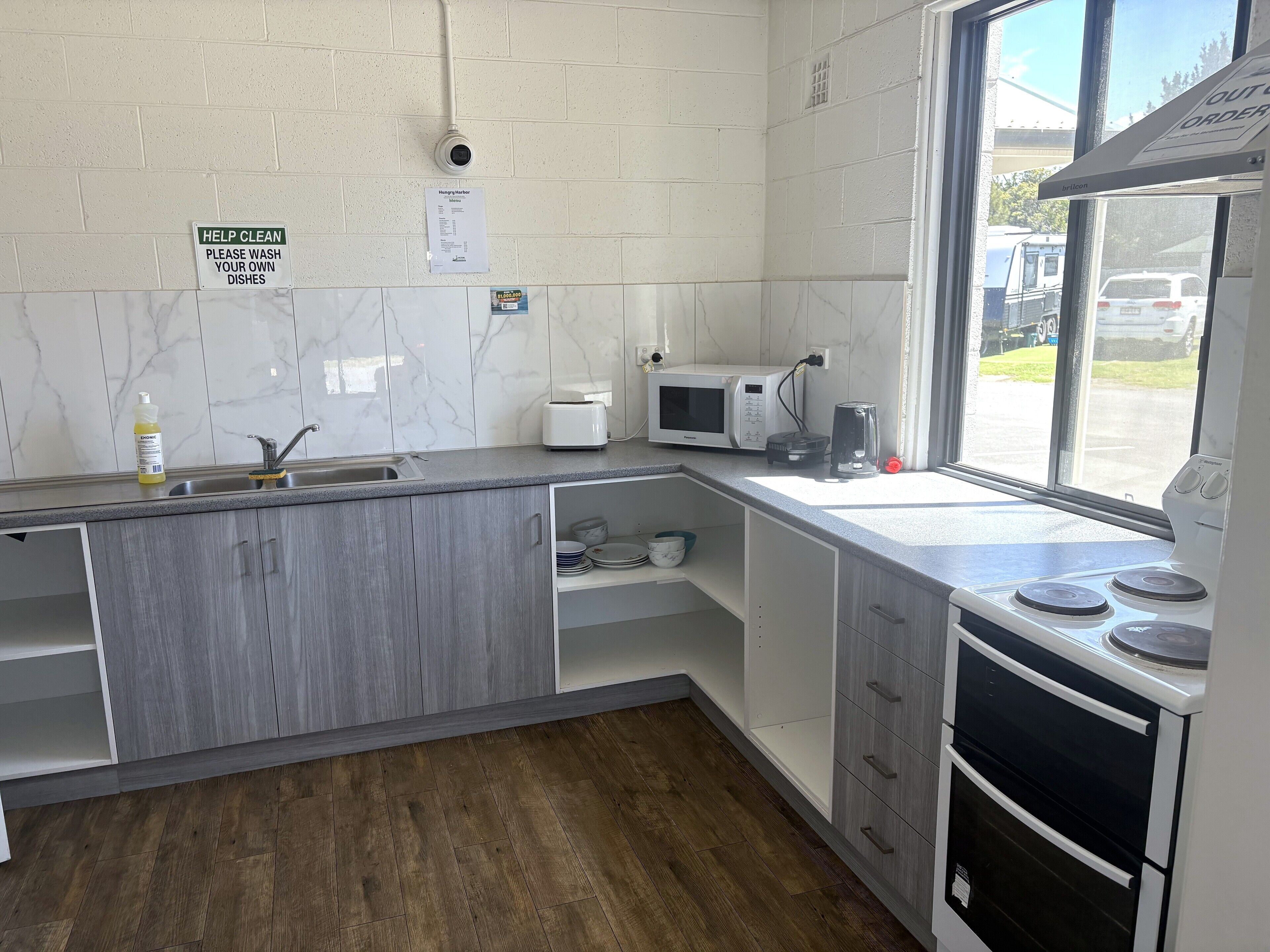 A modern kitchen with grey cabinets, a sink, a microwave, and a stove. There are signs on the wall and a window with a view of the outside.