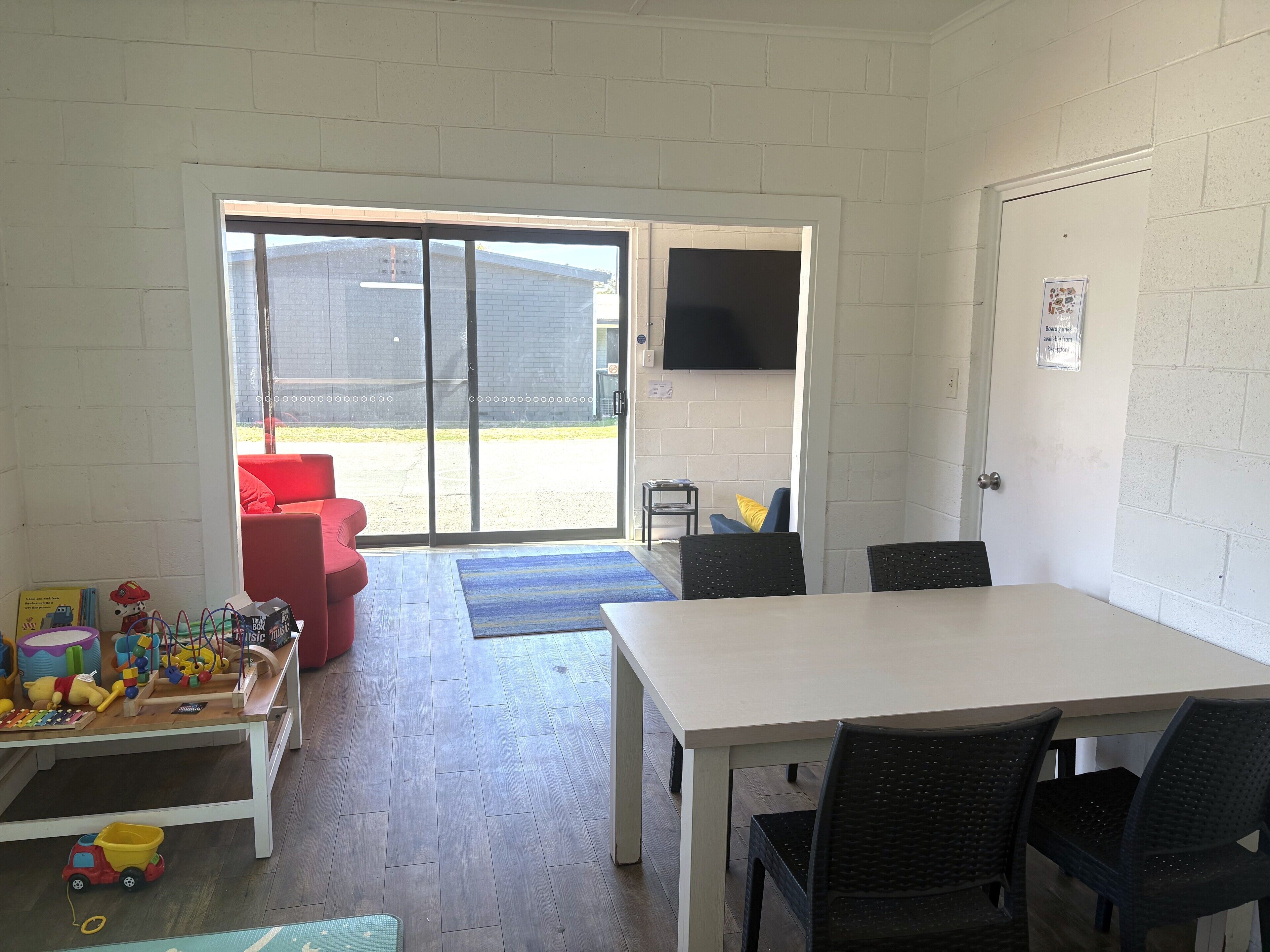 Una habitación con una mesa y sillas blancas, un sofá rojo, un tapete azul y un andador de trenes de juguete.