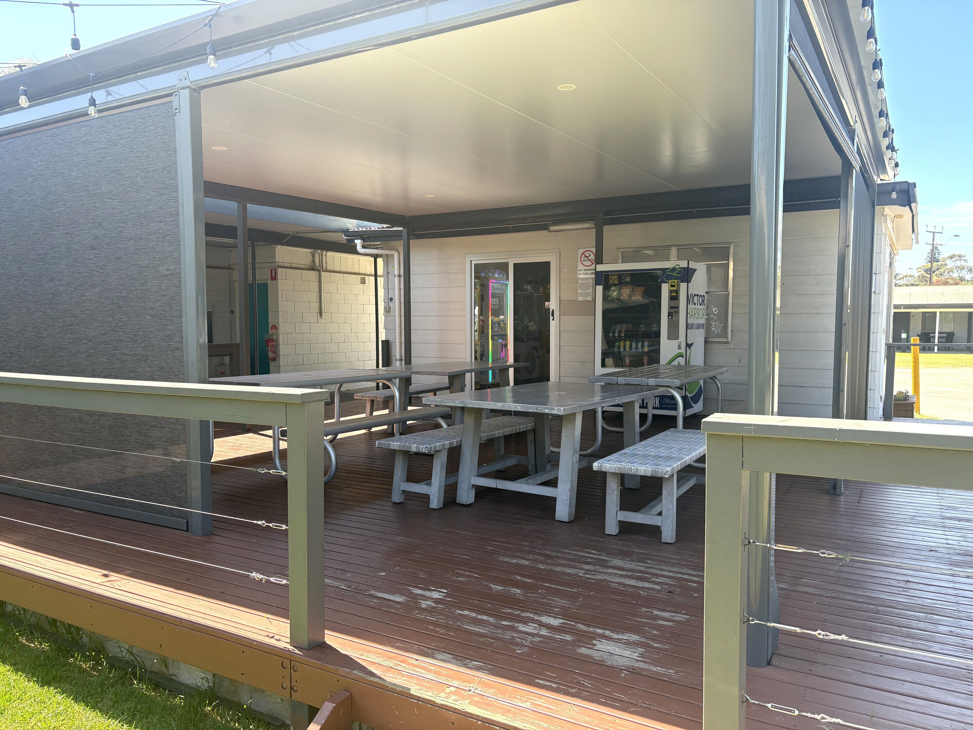 Un espace extérieur aménagé avec des tables de pique-nique et des bancs, un distributeur automatique et un espace de repos abrité.