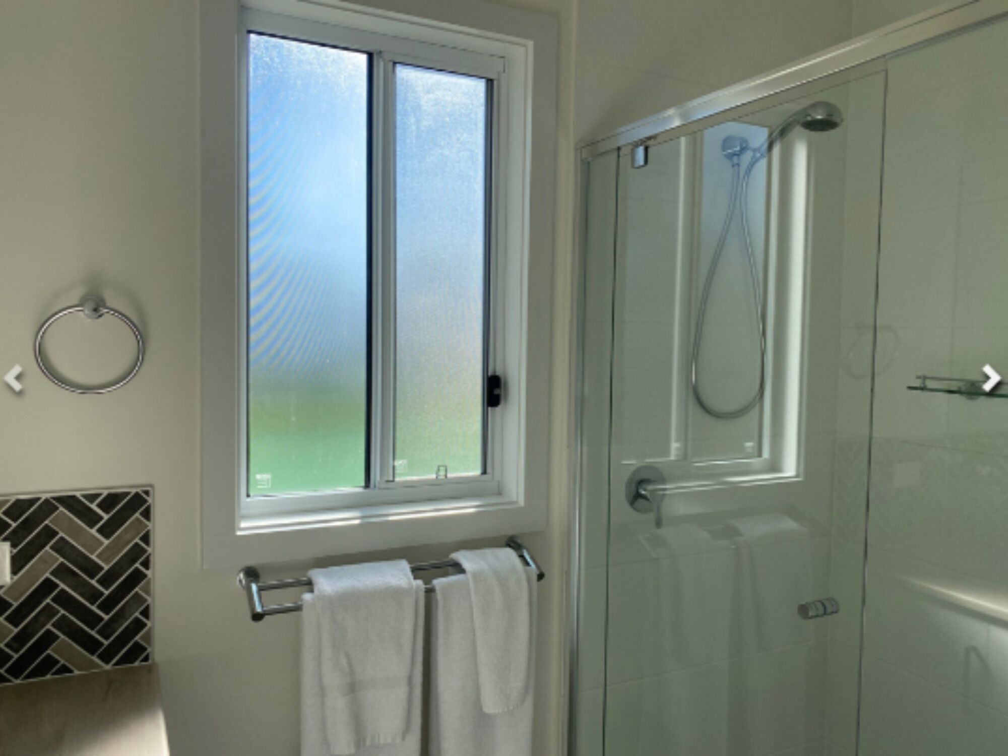 Une salle de bain avec une porte de douche en verre, une fenêtre à vitrage dépoli et un porte-serviettes avec deux serviettes.