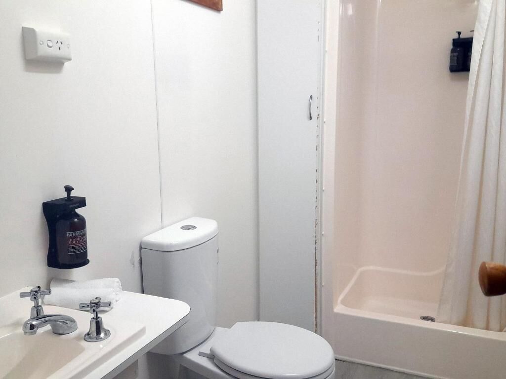 A small, compact bathroom with a white toilet, a sink with a soap dispenser, and a shower area.