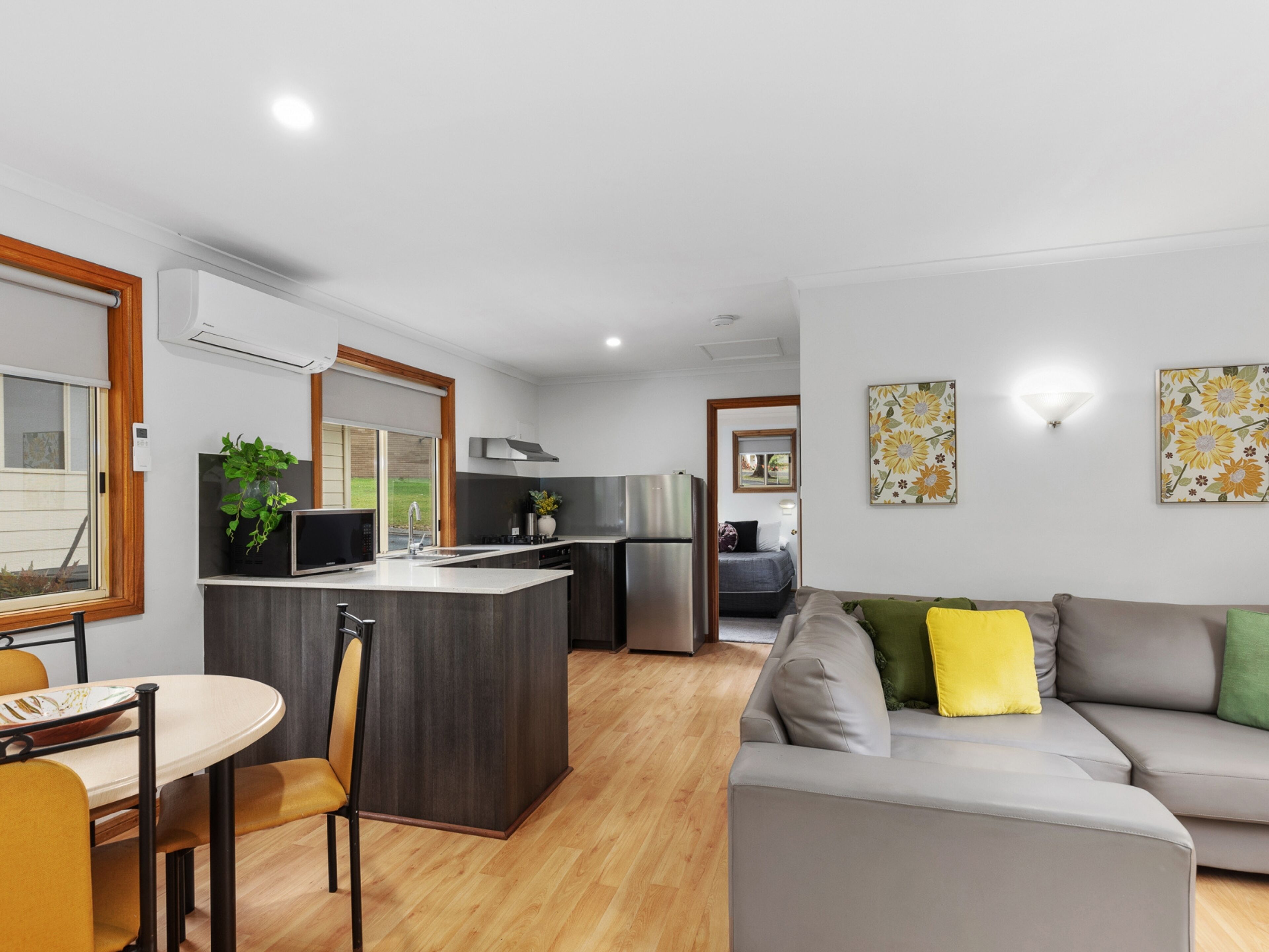 A modern kitchen with a central island, a dining area with a table and chairs, and a living room with a sofa and cushions.