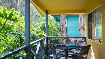 A covered outdoor area with a table and chairs, surrounded by lush greenery.