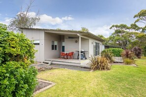 A single-story house with a covered porch, a small patio with red chairs, and a variety of plants in the yard. - Blue Lake Holiday Park  (Mount Gambier)
