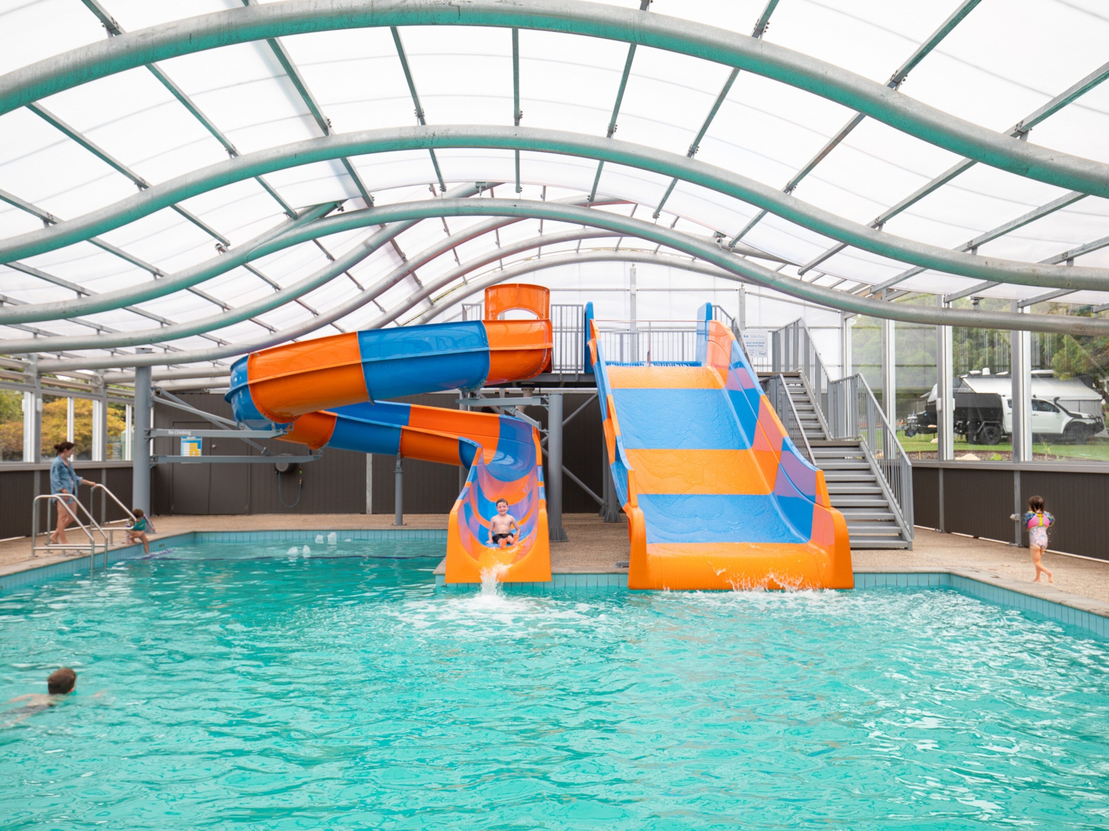 Una piscina techada con tobogán de agua y estructura de techo cubierto.