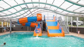 Una piscina techada con tobogán de agua y estructura de techo cubierto.