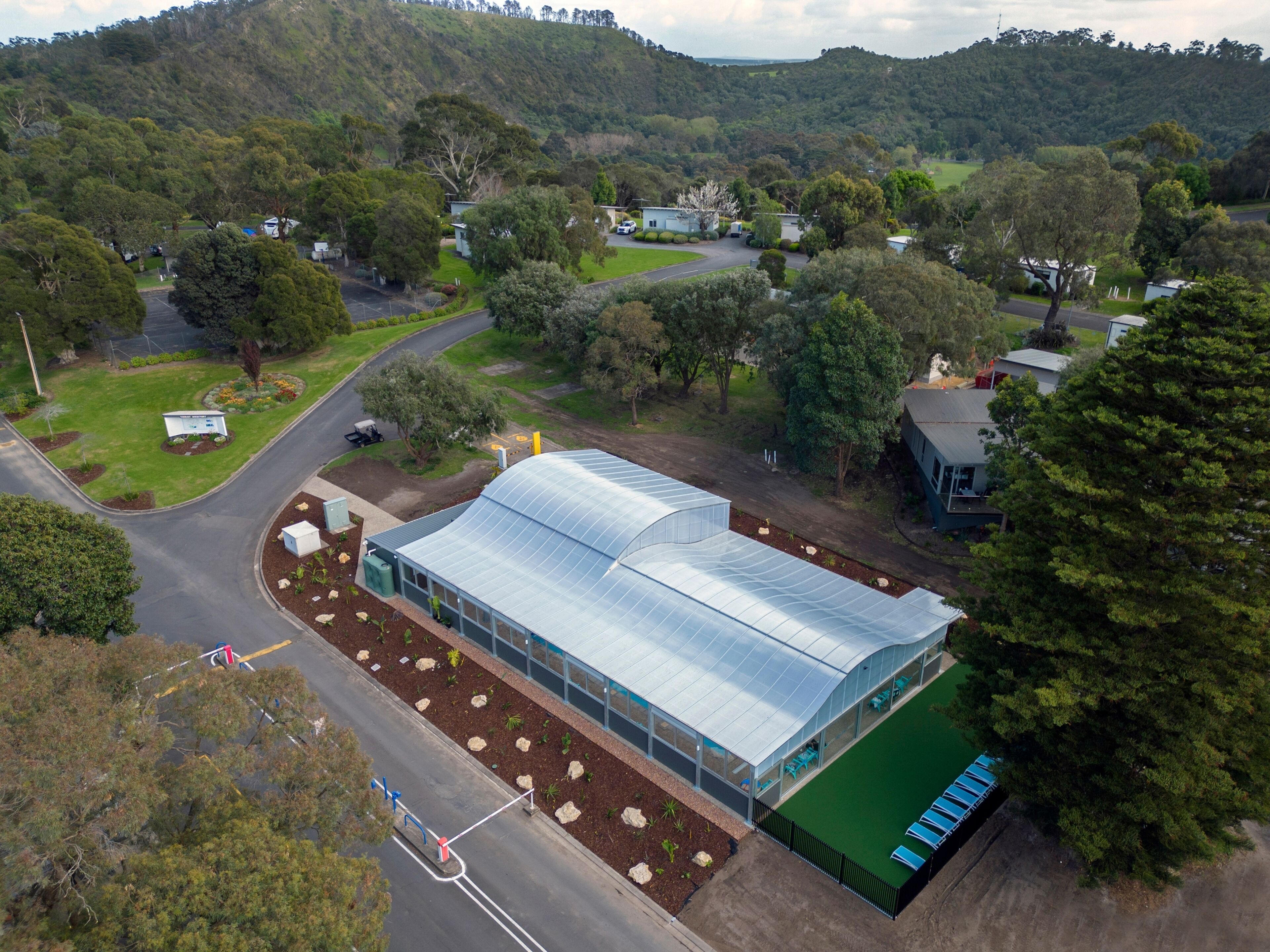 A large greenhouse with a curved roof, surrounded by a well-maintained lawn and a parking area.