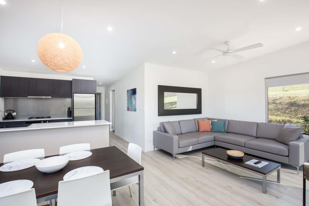 A modern living space with a dining area, a gray sectional sofa, a coffee table, and a kitchen with dark cabinets.