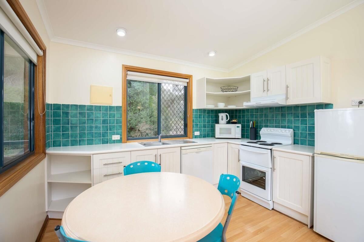 A compact kitchen with white cabinets, a microwave, a stove, and a sink. There is a window with a view of greenery outside.