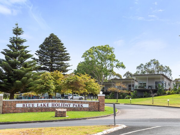 A sign for Blue Lake Holiday Park with a stone wall and a grassy area. - Blue Lake Holiday Park  (Mount Gambier)