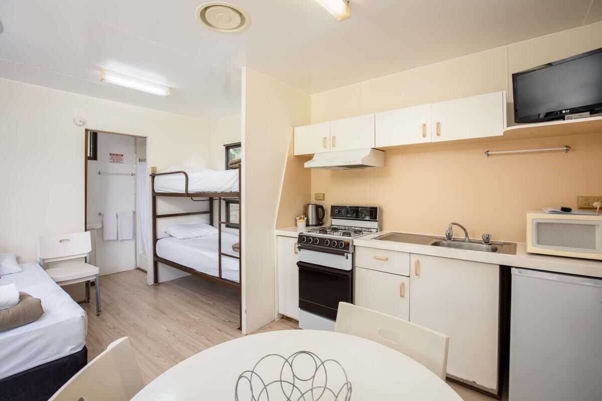 A compact hotel room with a bunk bed, kitchenette, and a small dining table.
