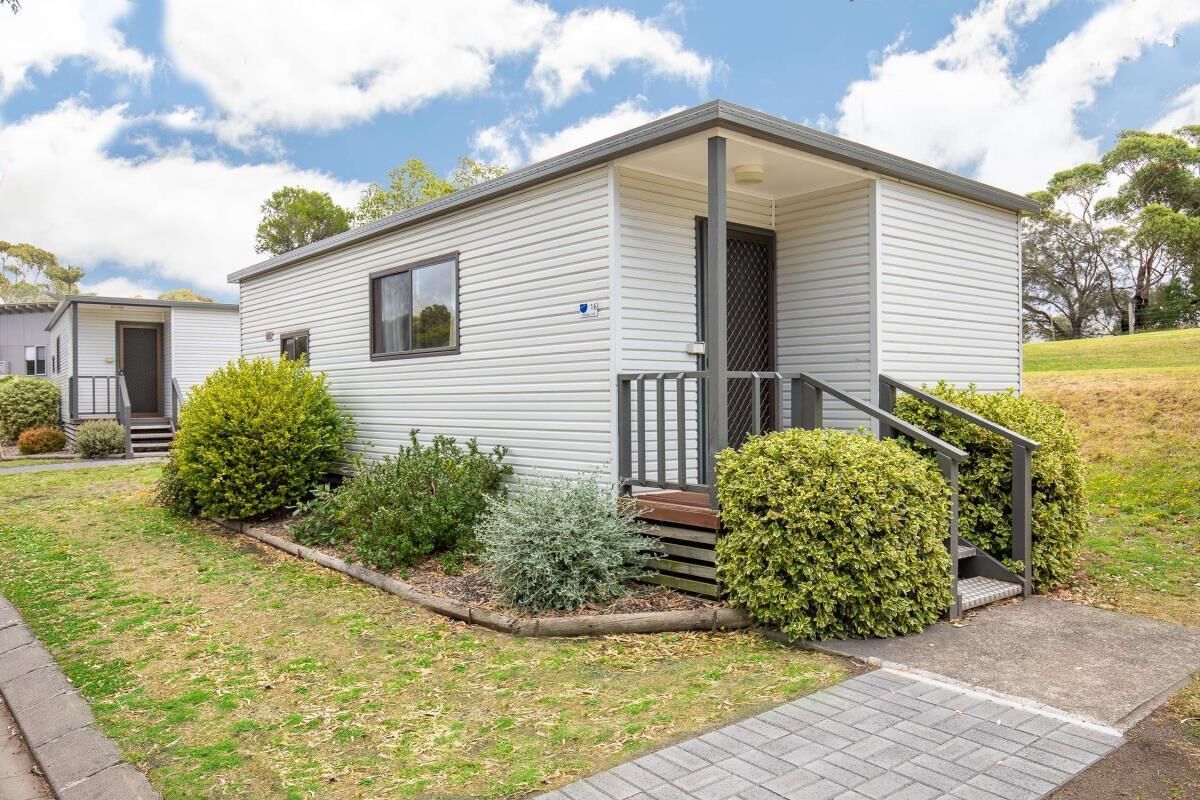 A single-story mobile home with a front porch, a small staircase, and a well-maintained lawn with various shrubs.