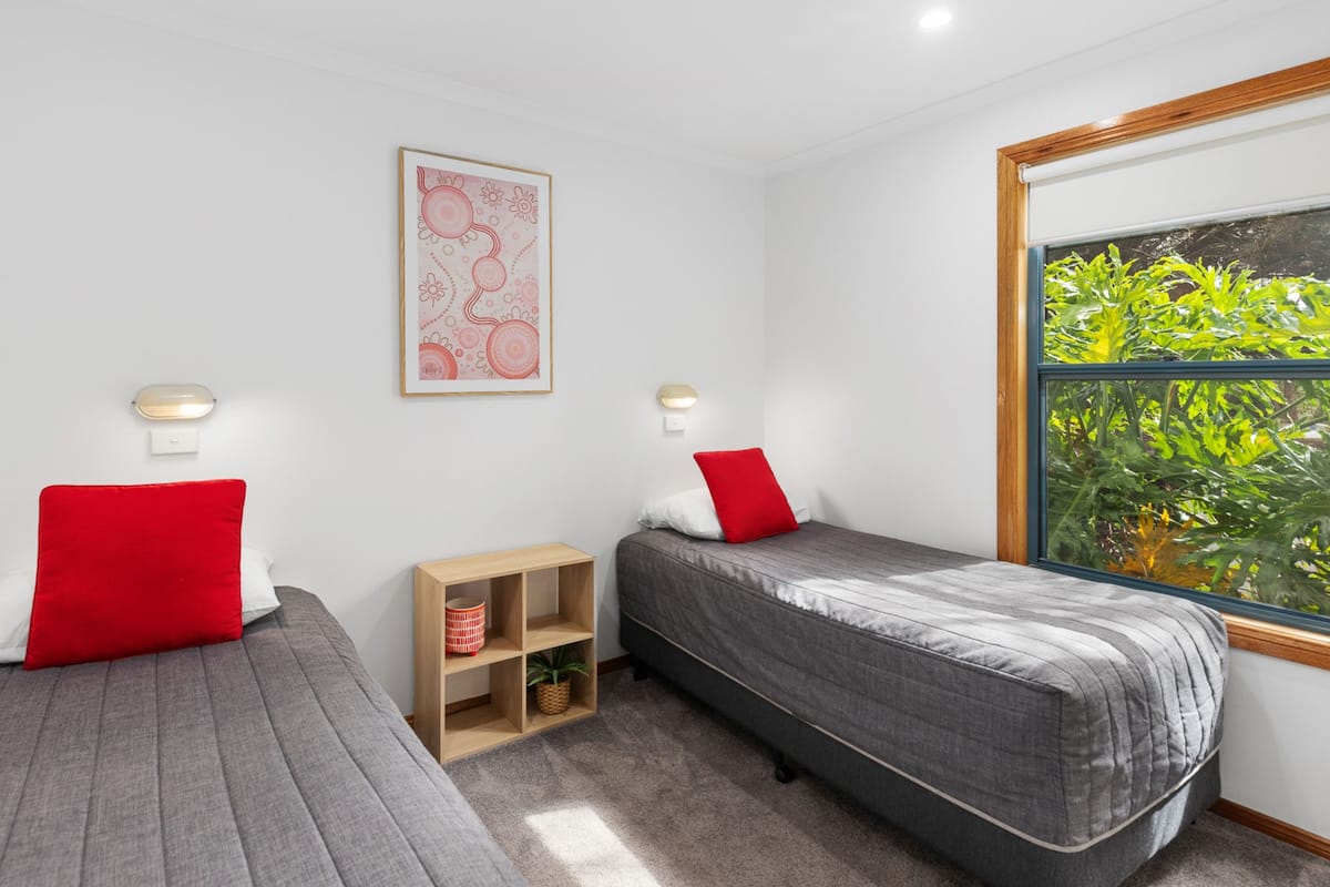 Ein Schlafzimmer mit zwei Betten, einer kleinen Holzablage und einem Fenster mit Blick ins Grüne.