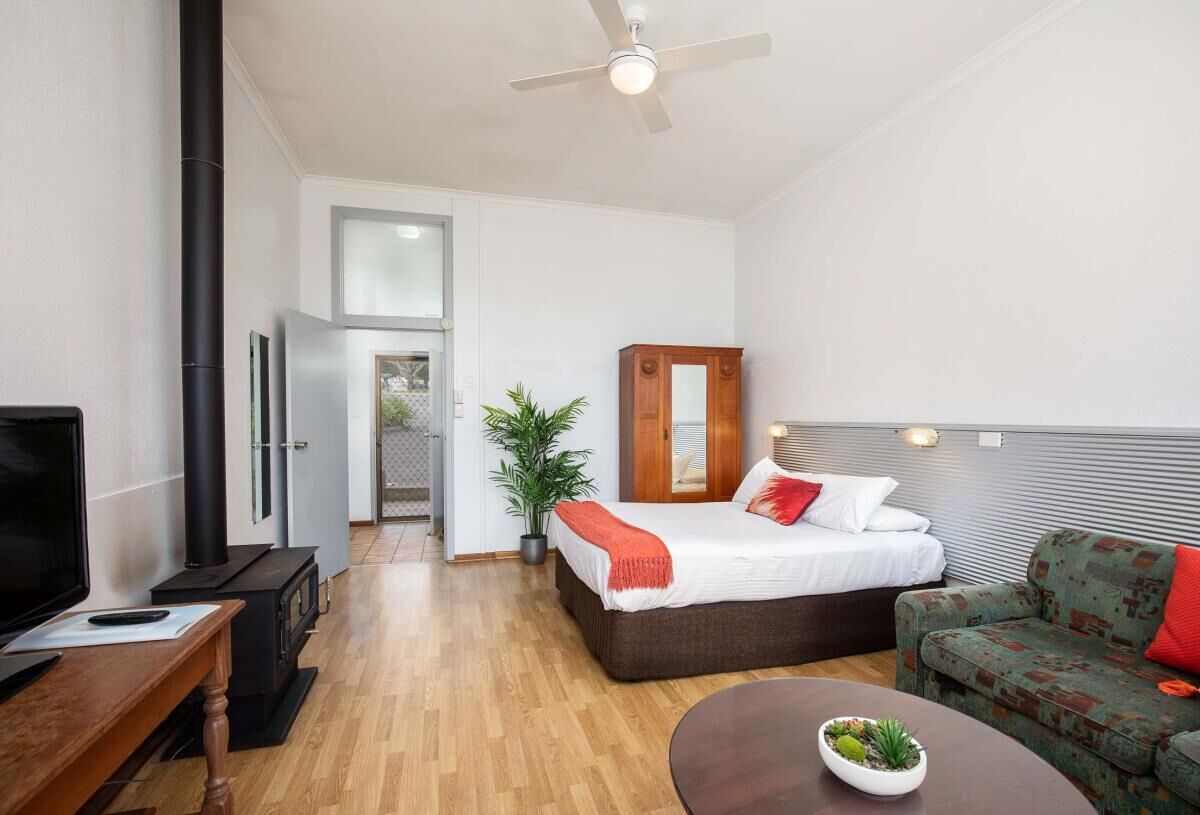 A modern hotel room with a bed, a sofa, a TV, a fireplace, and a ceiling fan.