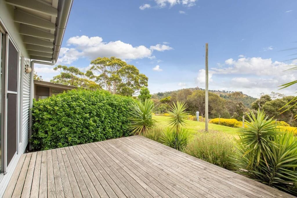 A wooden deck with a view of a landscaped garden and distant hills.