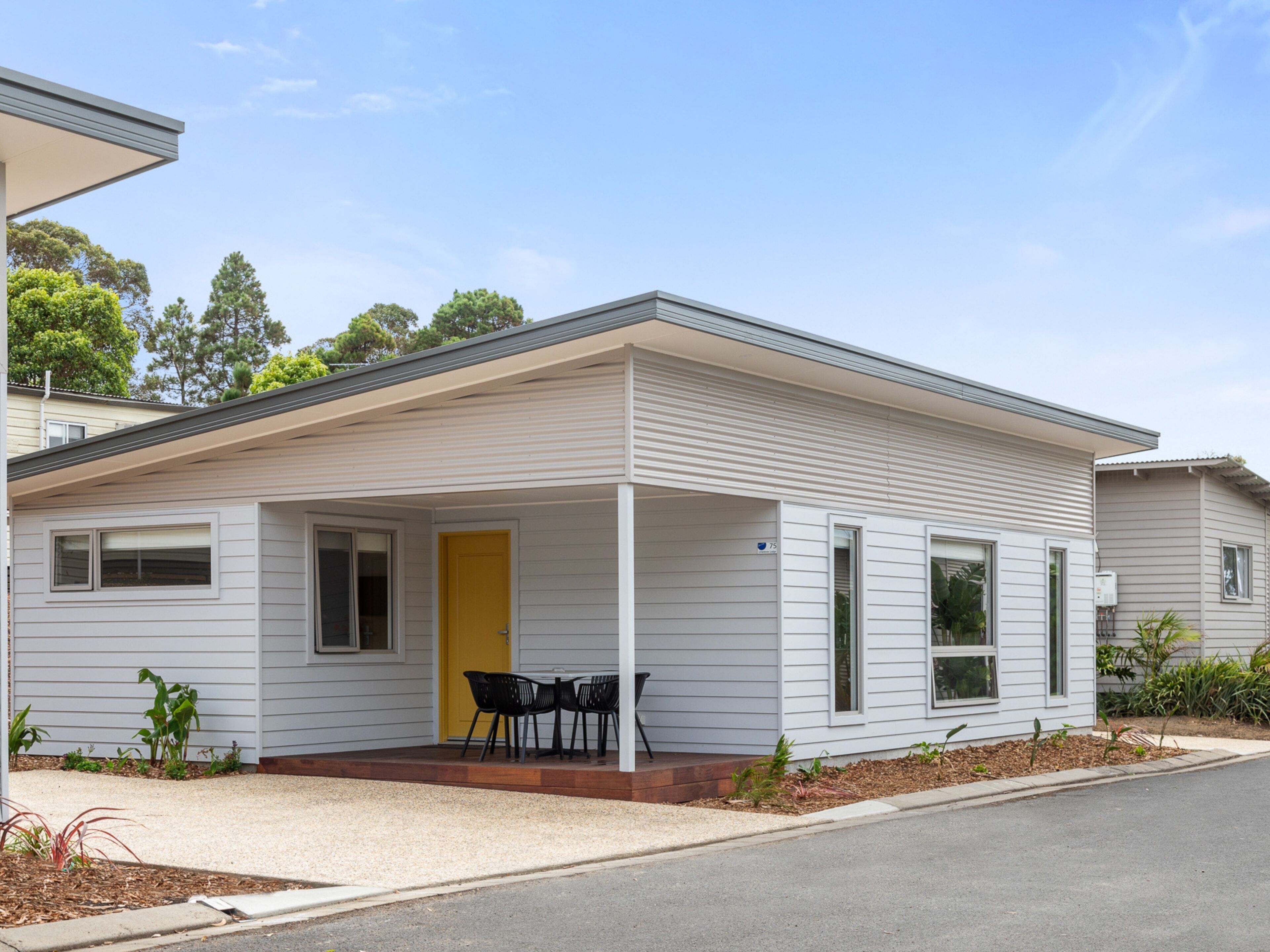 A single-story house with a covered porch, a yellow door, and a small outdoor seating area.